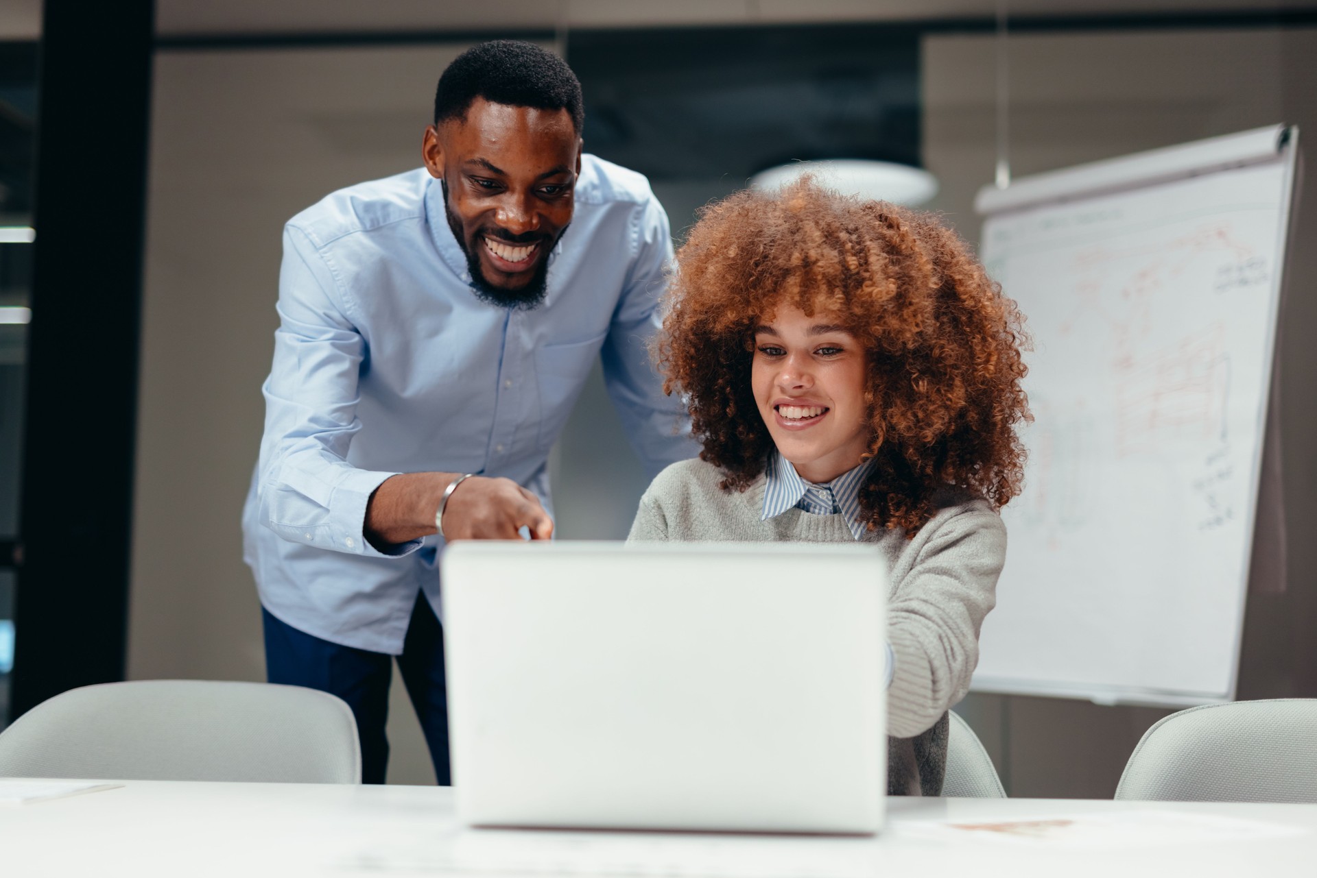 Two smiling business people looking at laptop and working together in modern office