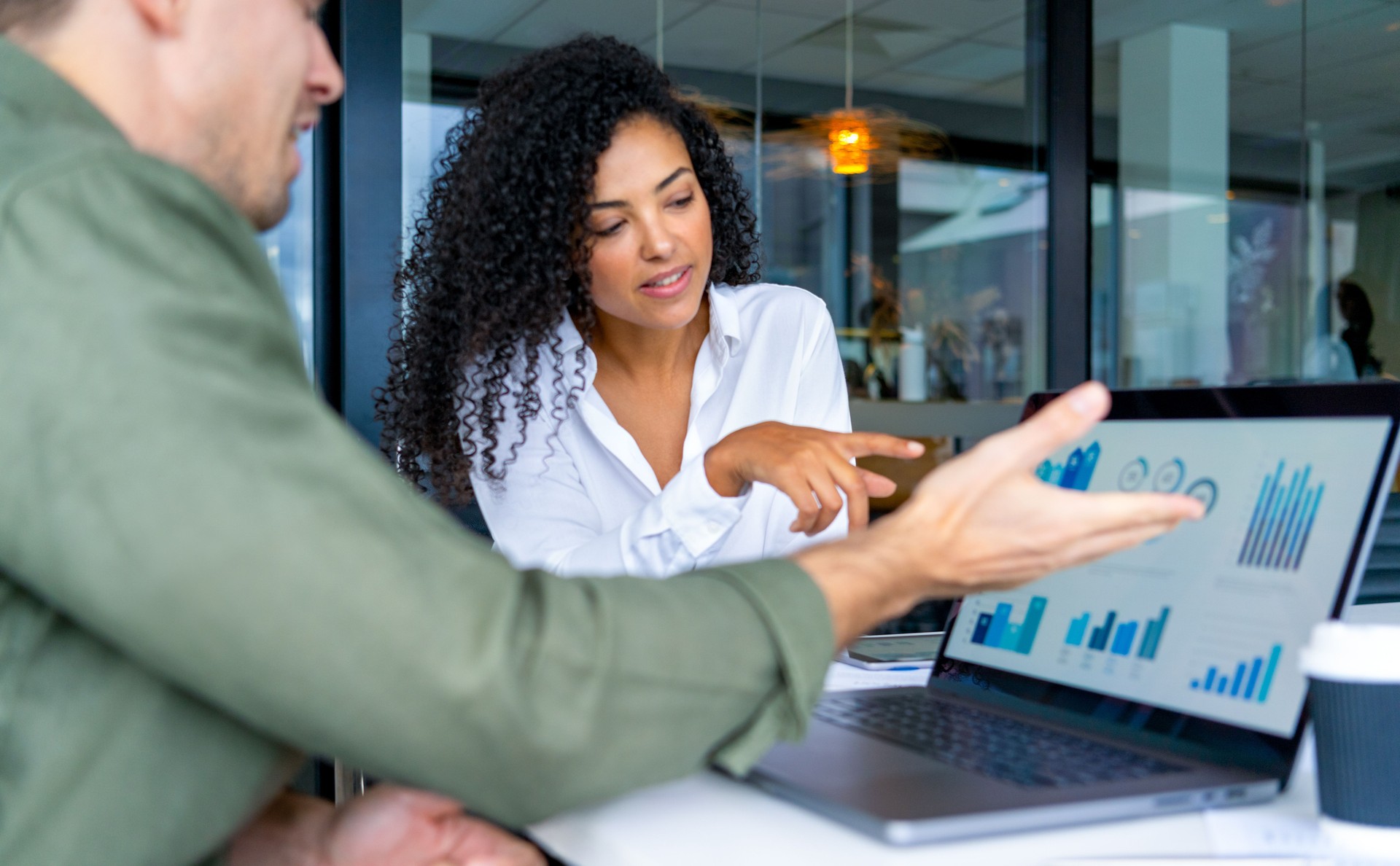Business man and business woman in a meeting at the office. There is a laptop on the table  showing finance charts and graphs.